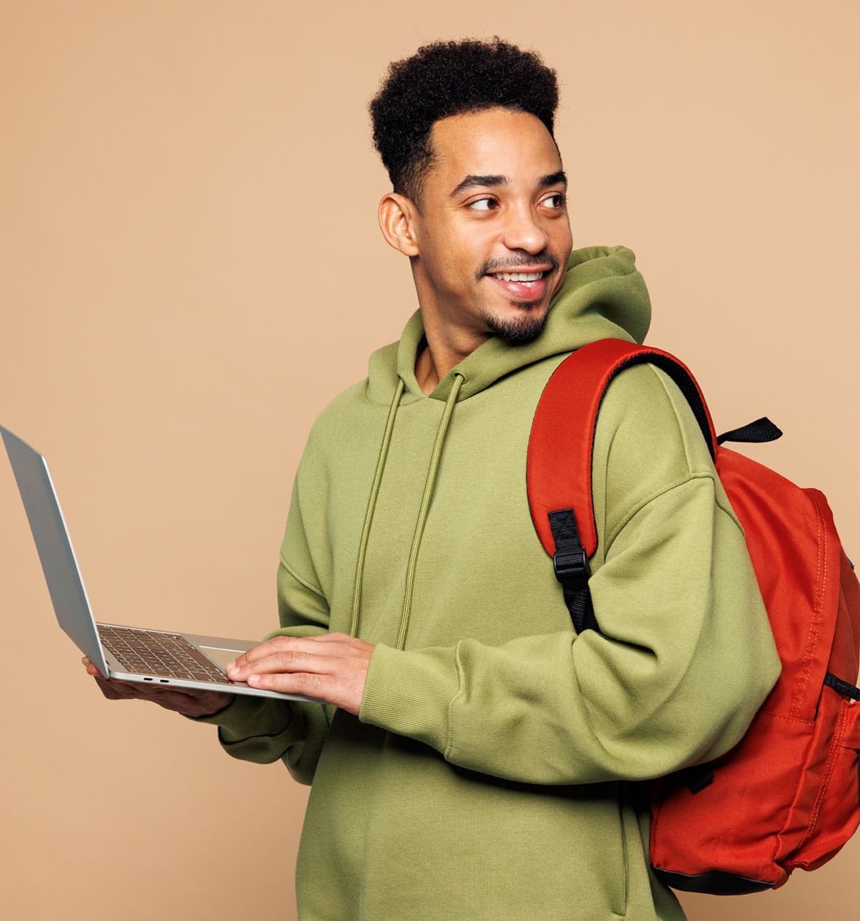 Smiling young man with backpack using laptop on beige background.